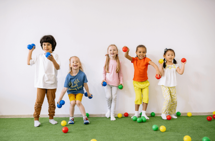 5 children having fun standing against a wall getting ready to throw some colourful balls.